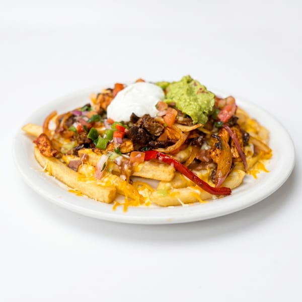 Loaded fries topped with cheese, meat, onions, peppers, guacamole, and sour cream on a white plate.